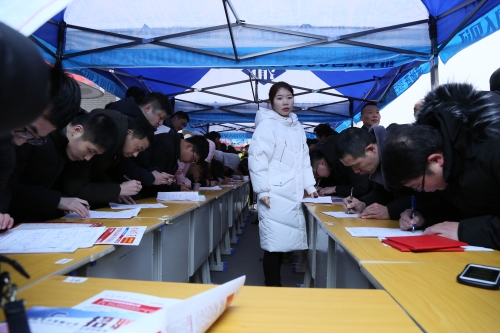 图为：泰兴市2019年新春人才招聘会暨人才交流洽谈会现场求职者在某集团公司摊位前填写报名表
